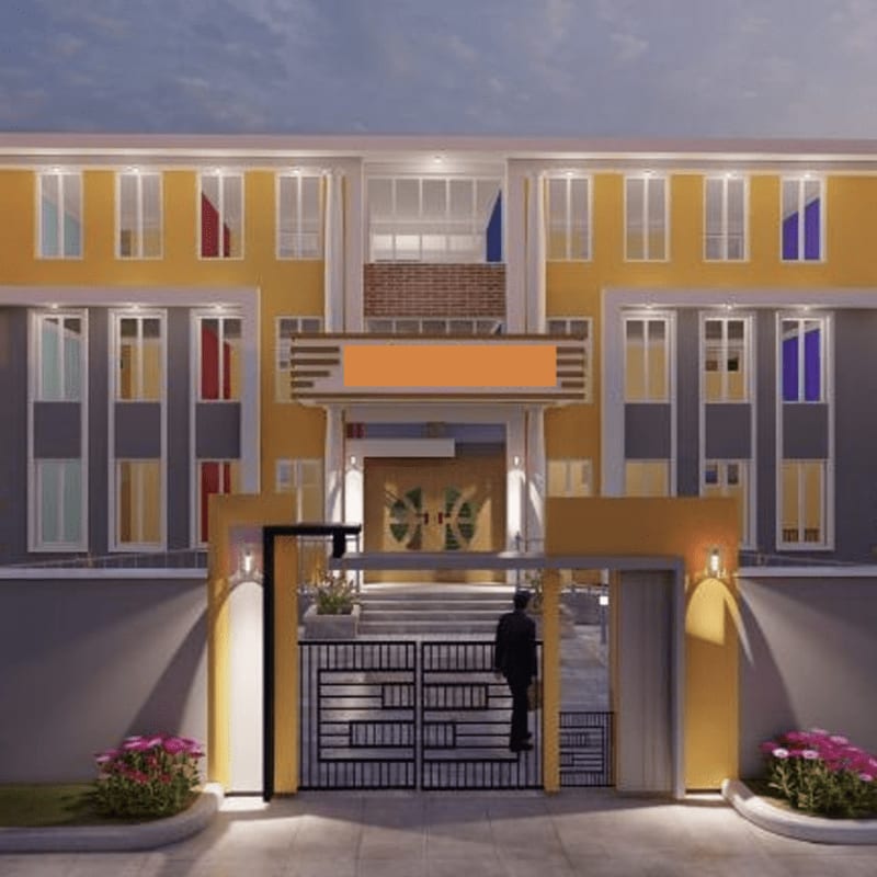 A man stands at the gate of a modern, multi-story building with yellow and gray facades, framed by flowering bushes.