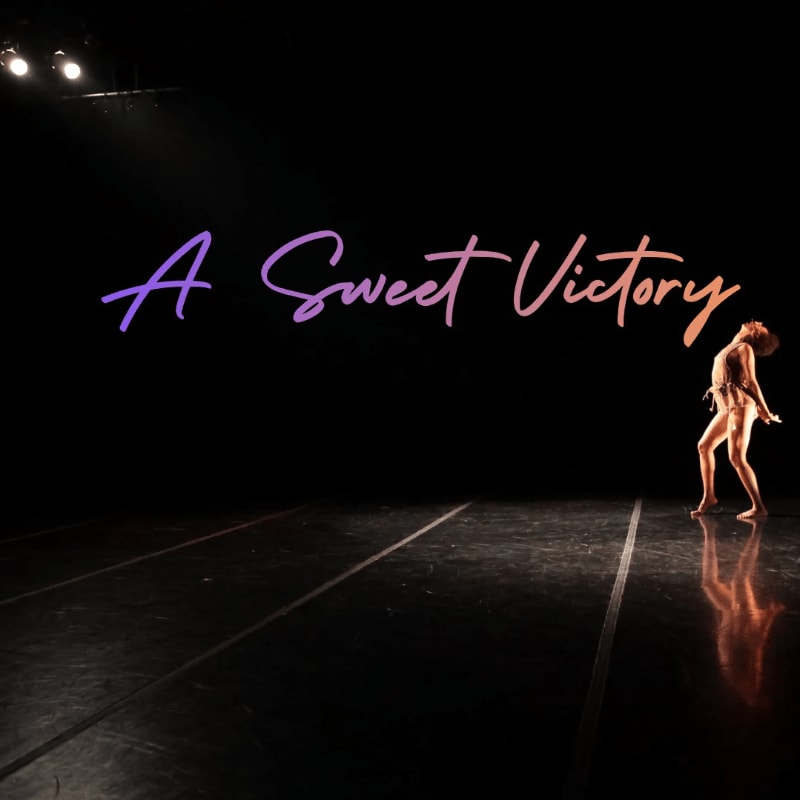 A lone dancer strikes a pose on a dark stage with the words "A Sweet Victory" projected in a gradient of purple and orange behind her.