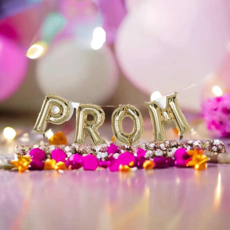 Golden "PROM" balloons float above a floral arrangement with bokeh lights and balloons in the background.