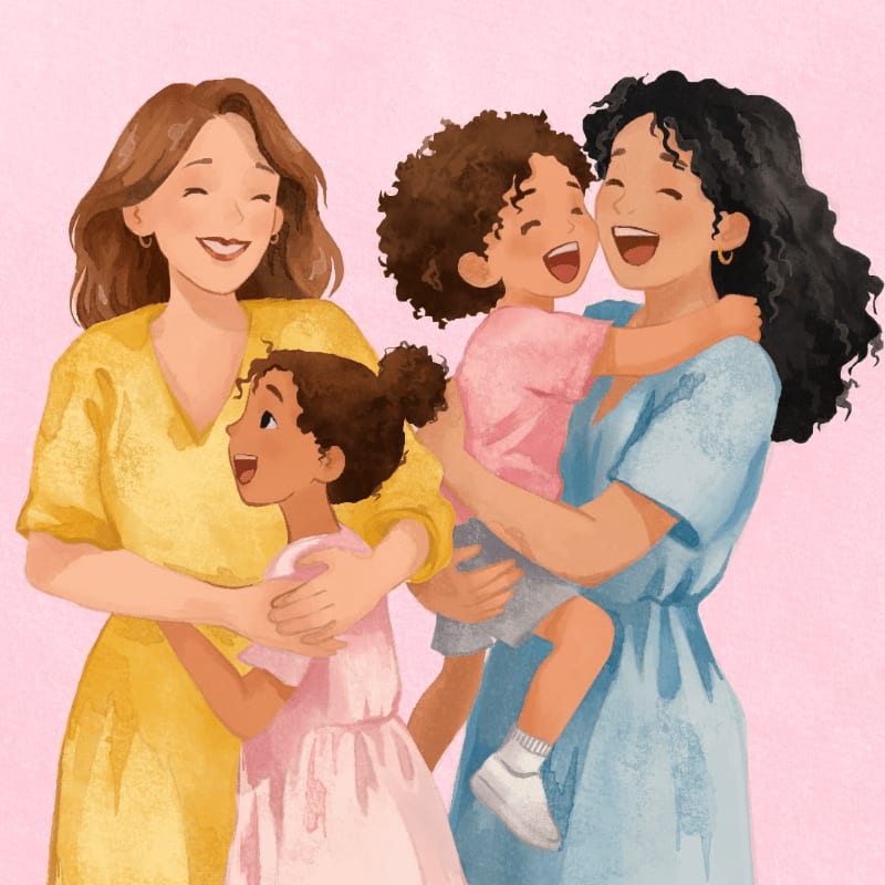 Two women embrace their two young daughters, all smiling joyfully against a soft pink background.