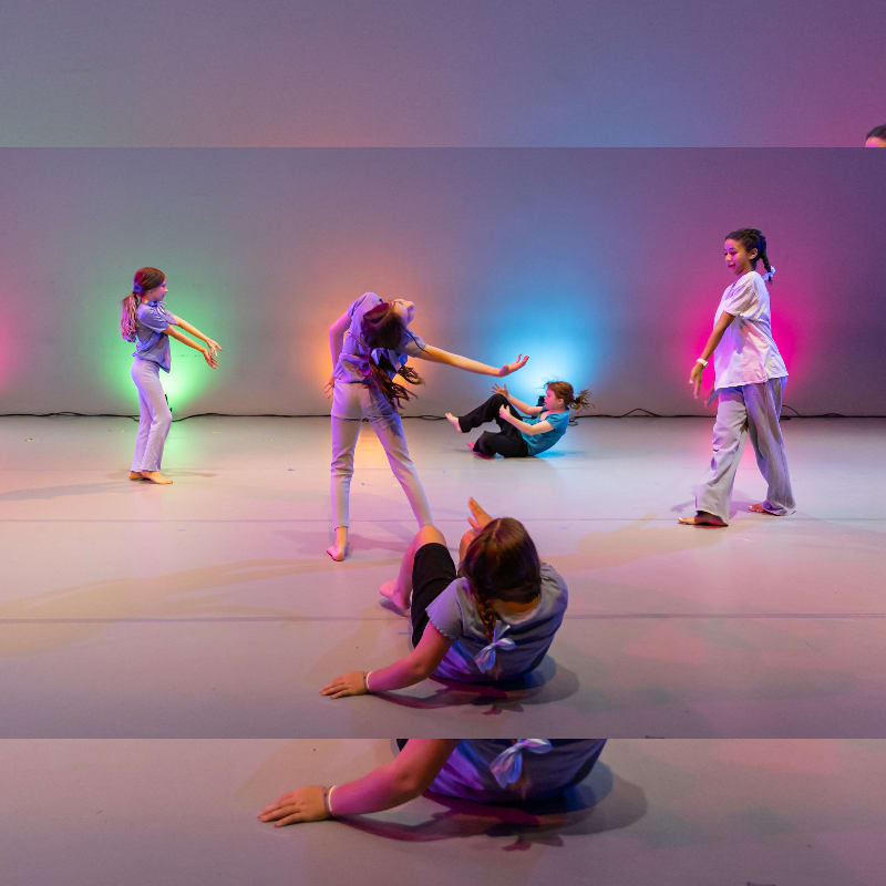 Several young dancers in purple and white outfits are performing on a stage with colorful lights in the background.