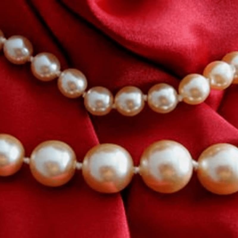 Two strands of pearls rest on a luxurious red satin background.