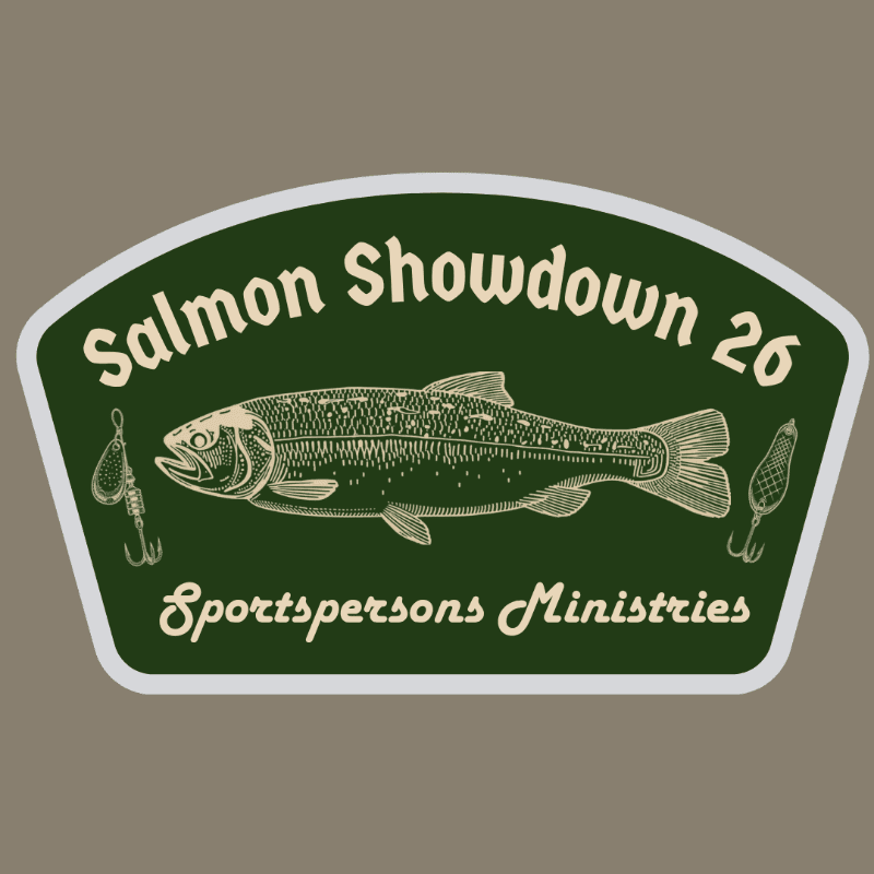 A detailed illustration of a salmon is centered on a dark green background with fishing lures on either side, all within a white-bordered, arched emblem that reads "Salmon Showdown 26" at the top and "Sportspersons Ministries" at the bottom, set against a muted brown backdrop.