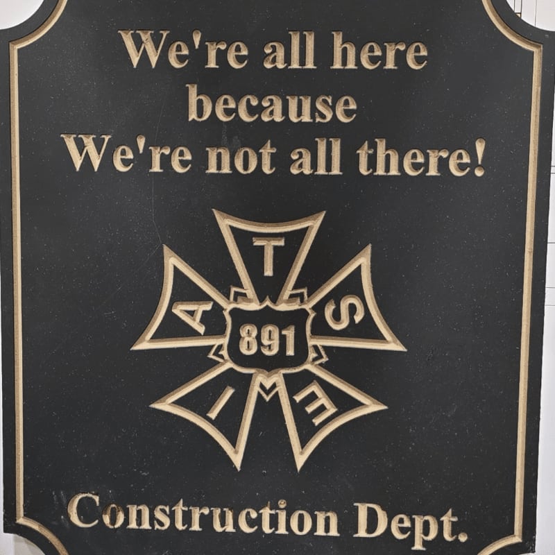 A black plaque with carved text and a crest is mounted on a white wall.