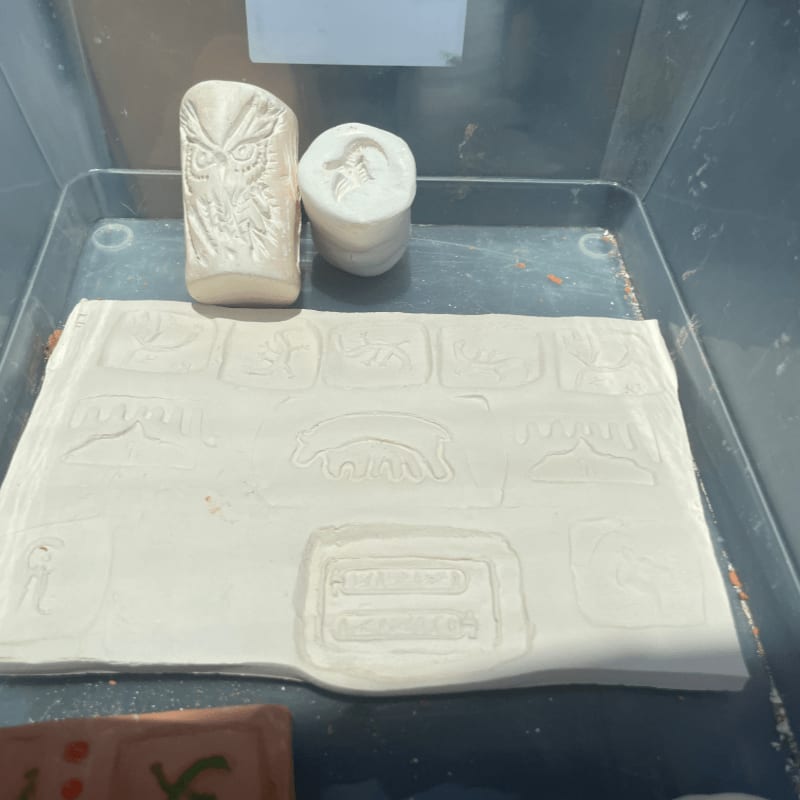Two clay molds, one with an owl and the other with a bear, sit on a tray with a larger clay slab imprinted with various animal designs in the foreground.
