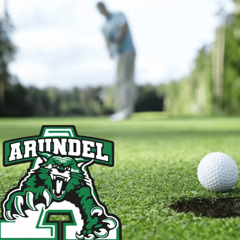 A green wildcat logo is in the foreground next to a golf ball on the edge of a hole, with a golfer in the blurred background on a sunny course.