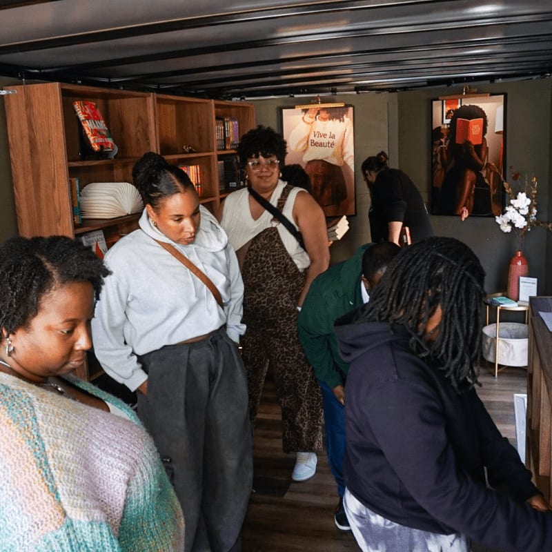 Several people browse books in a cozy shop with wooden shelves and artistic posters on the walls.