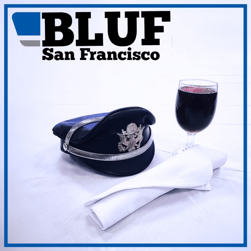 A dark blue cap with a silver emblem rests on a white napkin next to a glass of red wine, with the "BLUF San Francisco" logo in the background.