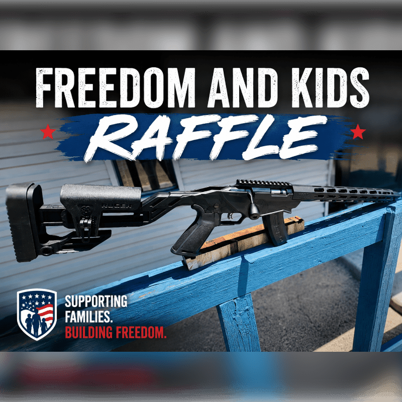 A rifle rests on a blue stand in the foreground, with the words "FREEDOM AND KIDS RAFFLE" and a logo in the background.
