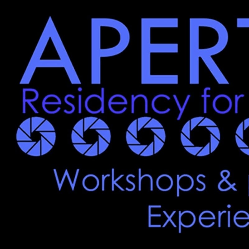 Large blue letters spelling "APERT" are in the foreground, with a row of camera aperture symbols below them, all set against a black background.
