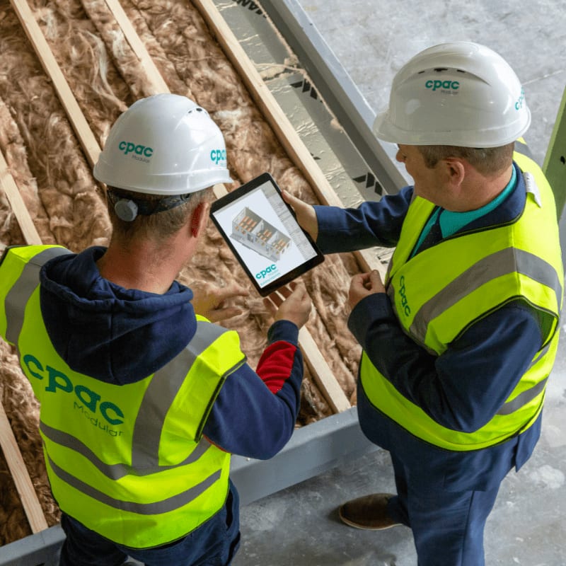 Two construction workers review plans on a tablet.