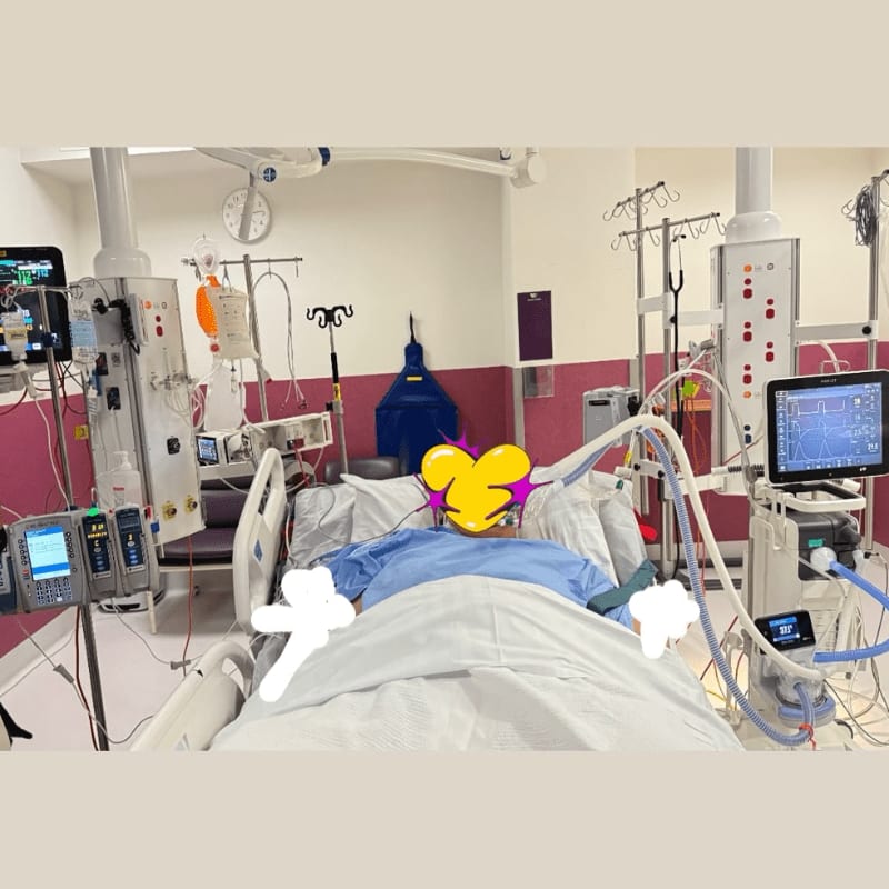 A patient lies in a hospital bed surrounded by medical equipment, with a ventilator and monitors visible in the background.