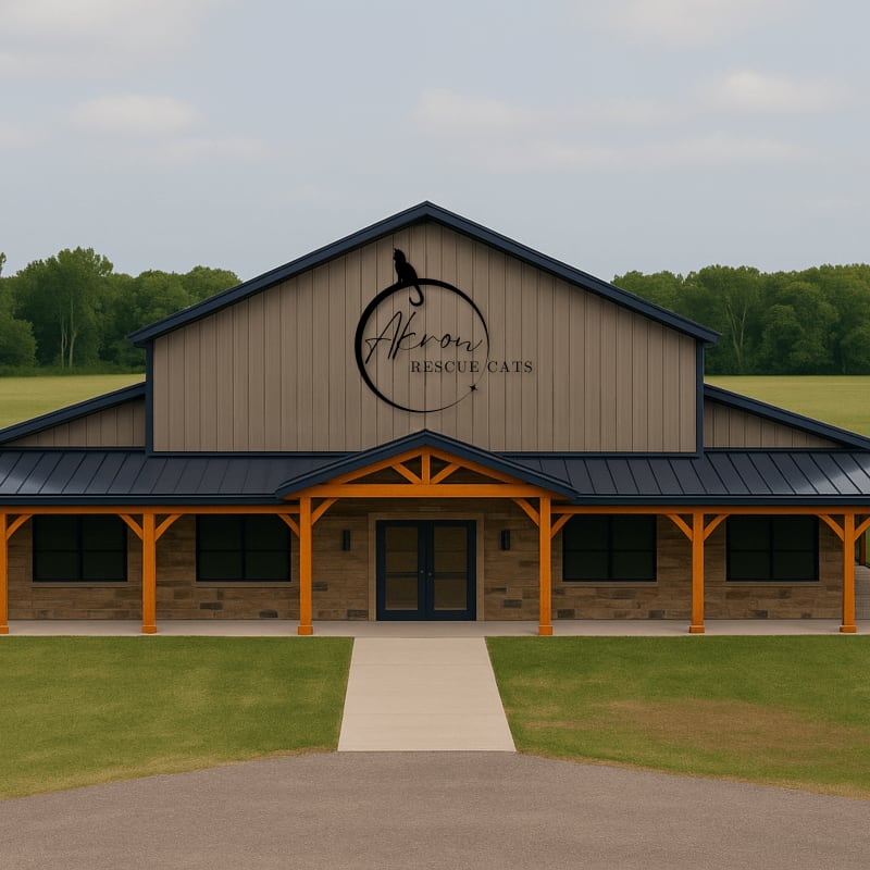 A modern tan building with a dark roof and stone accents, featuring a prominent "Akron Rescue Cats" logo, stands on a manicured lawn with a paved walkway leading to the entrance, all set against a backdrop of lush green trees under a cloudy sky.
