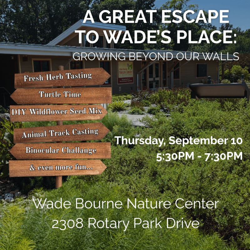 Wooden signs with event activities stand in the lush green foreground, with the Wade Bourne Nature Center building visible in the background.