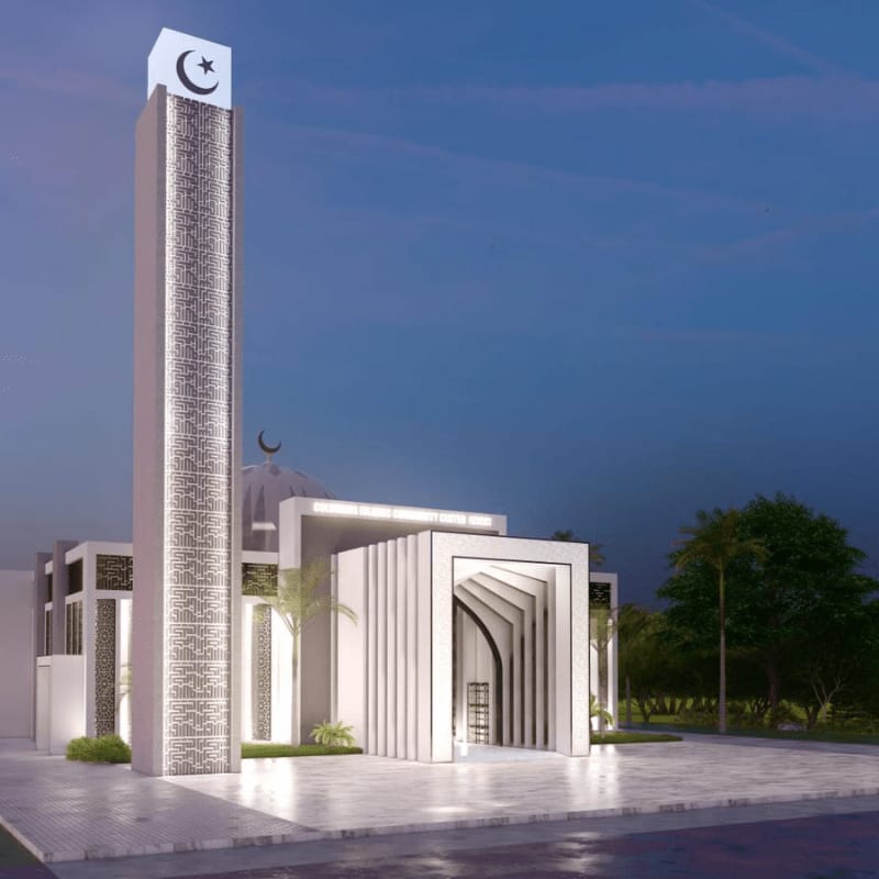 A modern mosque with a tall, illuminated minaret stands on a paved plaza, with trees and a twilight sky in the background.