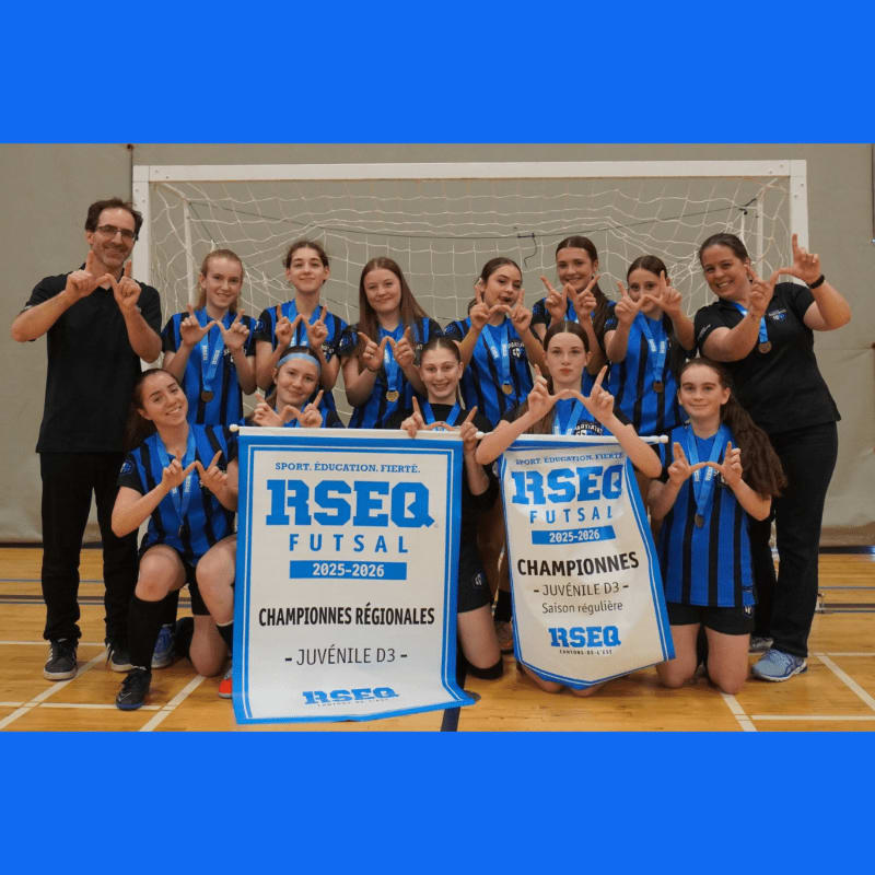 A girls' futsal team poses with championship banners and medals in front of a goal, with coaches on either side.