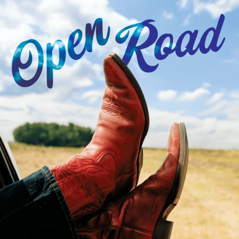 Red cowboy boots rest on a car window frame against a backdrop of a vast, open landscape under a cloudy sky with the words "Open Road" emblazoned above.