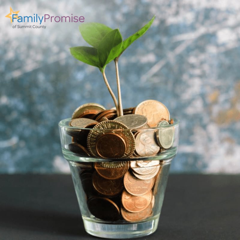 A small plant sprouts from a glass filled with coins, set against a textured, mottled blue and gray background.