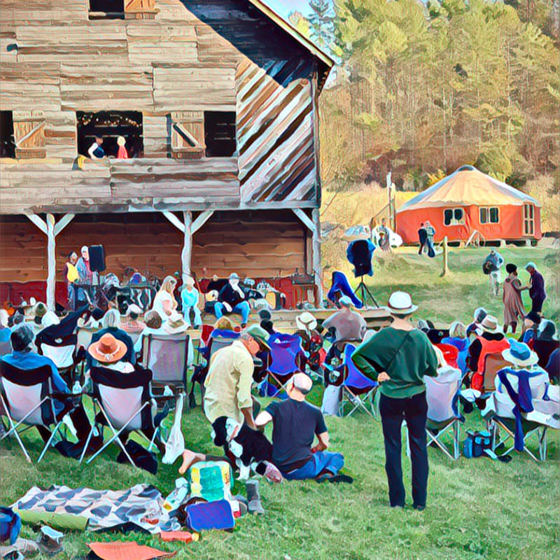 People are gathered on a grassy field in front of a rustic barn and a red yurt, with a wooded hillside in the background.
