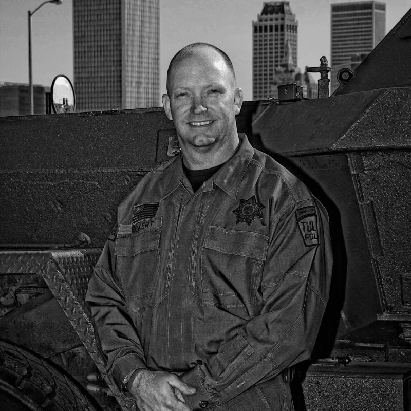 A smiling man in uniform stands in front of a large vehicle with a city skyline in the background.
