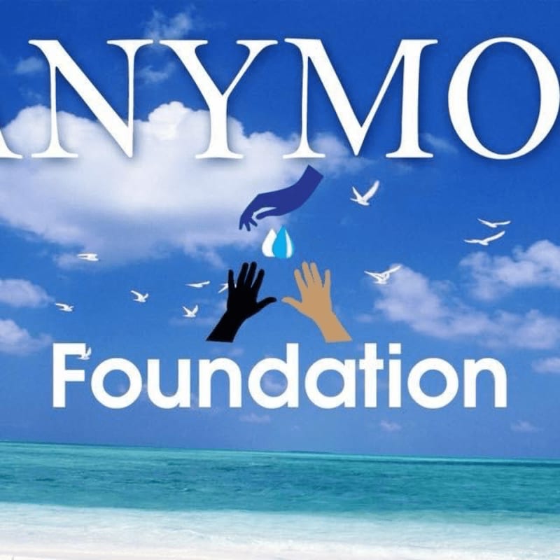 In the foreground, three hands reach up towards a falling drop of water against a bright blue sky with white clouds and birds, while the background features a serene ocean and sandy beach.