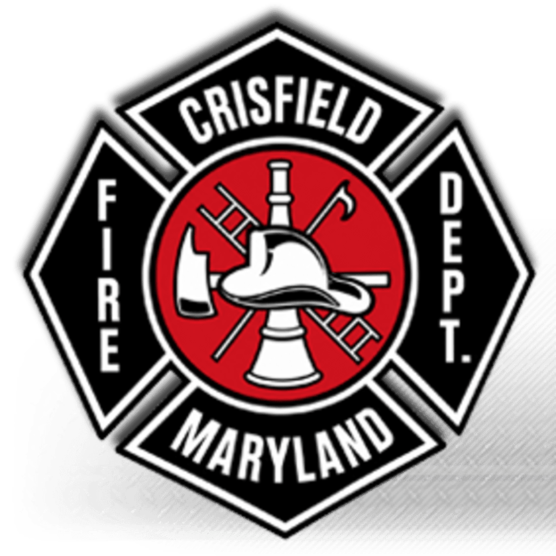 A Maltese cross emblem for the Crisfield Fire Department in Maryland, featuring firefighting tools and a helmet in the center, is set against a blurred, textured background.