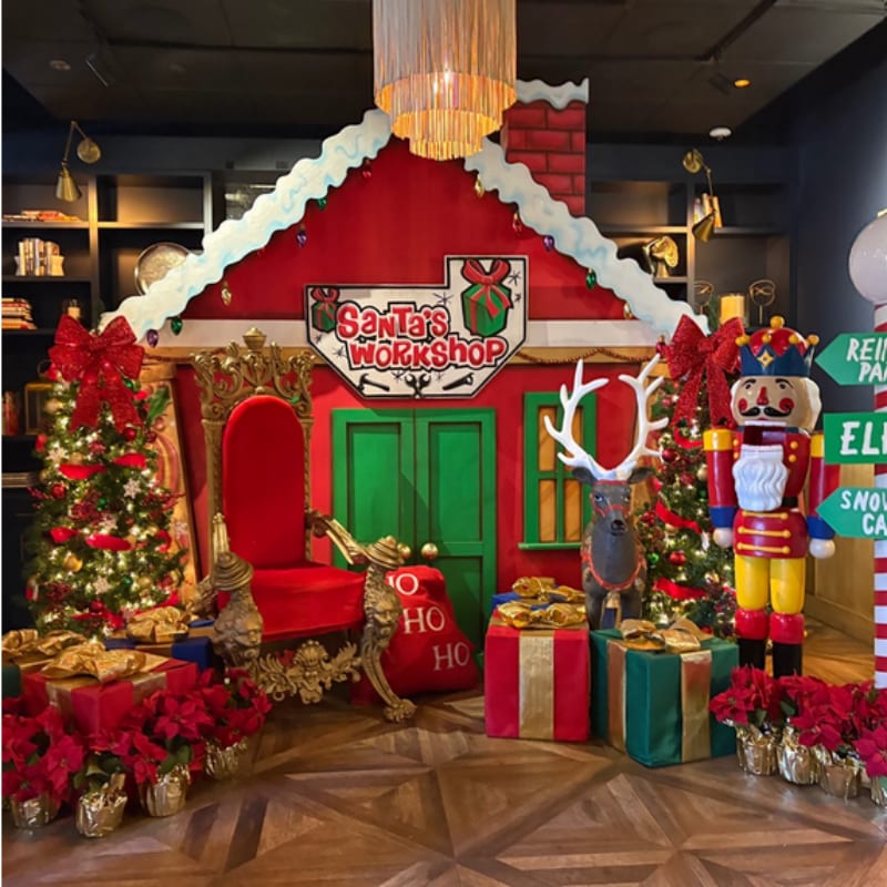 A festive Santa's workshop scene with a throne and Christmas trees in the foreground is set against a backdrop of shelves filled with items.