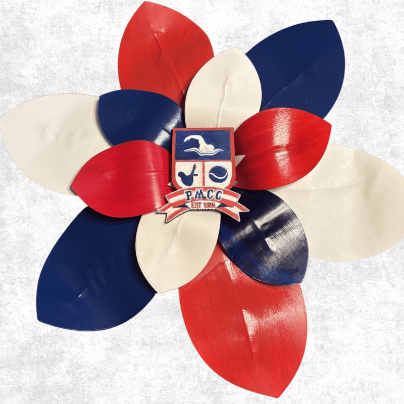A flower-like arrangement of red, white, and blue leaves surrounds a crest with the letters "P.M.C.C." against a textured gray background.