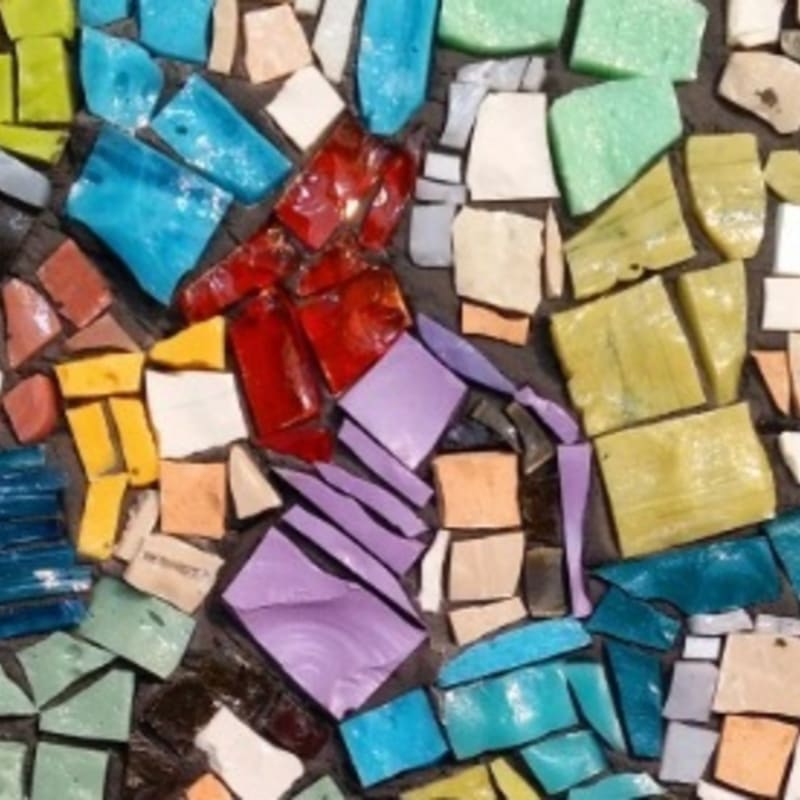 A mosaic of colorful, irregularly shaped glass shards in shades of blue, green, red, yellow, and purple fills the frame, with a dark, textured background visible between the pieces.