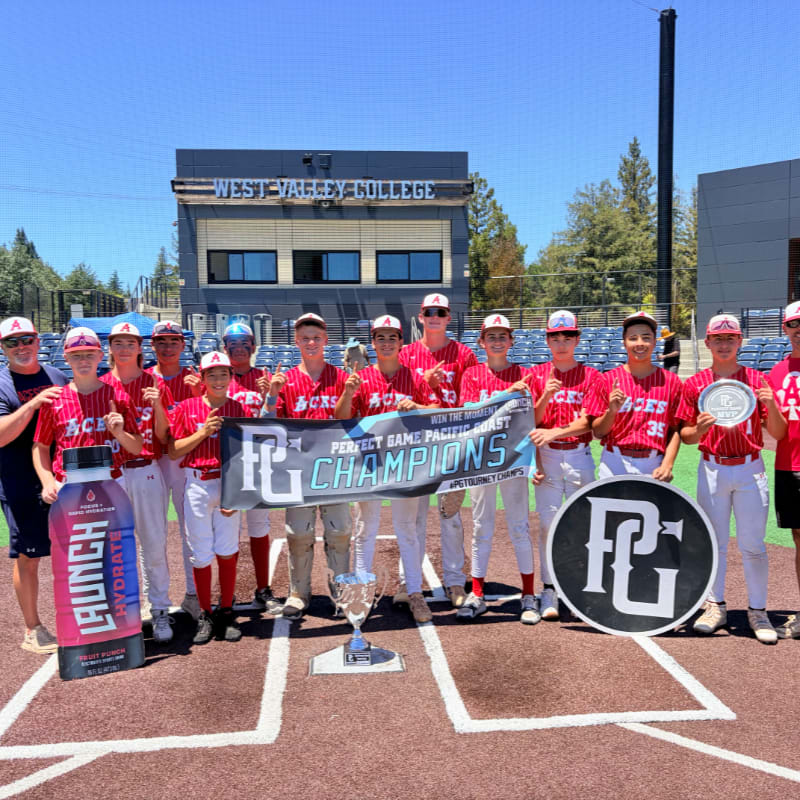 A baseball team poses with a championship banner and trophies in front of a college building.
