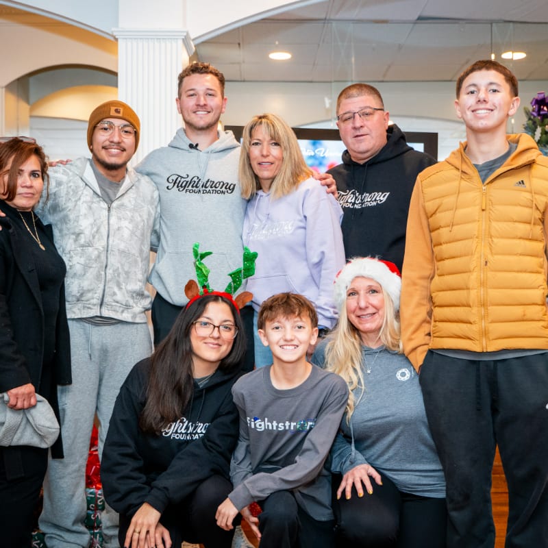 A group of nine people, some wearing festive headwear, pose for a photo in front of a blurred indoor background.