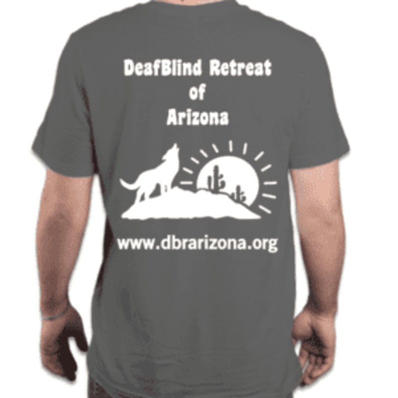 A person wears a dark gray t-shirt with a white graphic on the back featuring a howling wolf, cacti, and a sun, along with text for "DeafBlind Retreat of Arizona" and a website address.