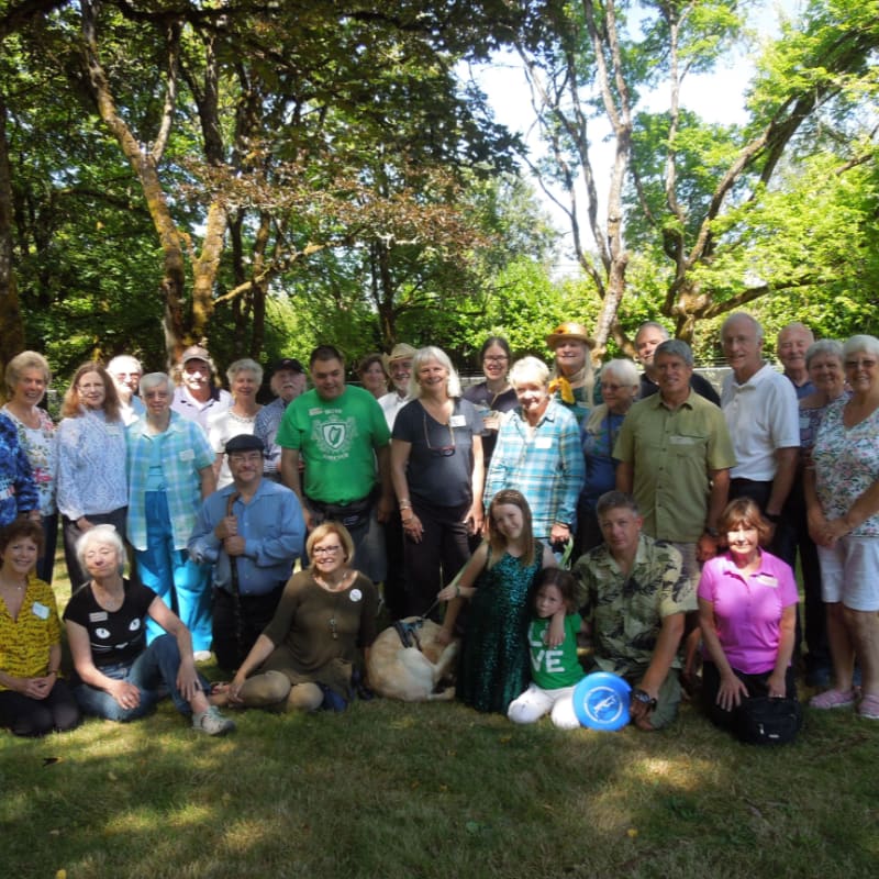 A group of people and a dog pose for a photo on a grassy lawn in front of a backdrop of lush green trees.