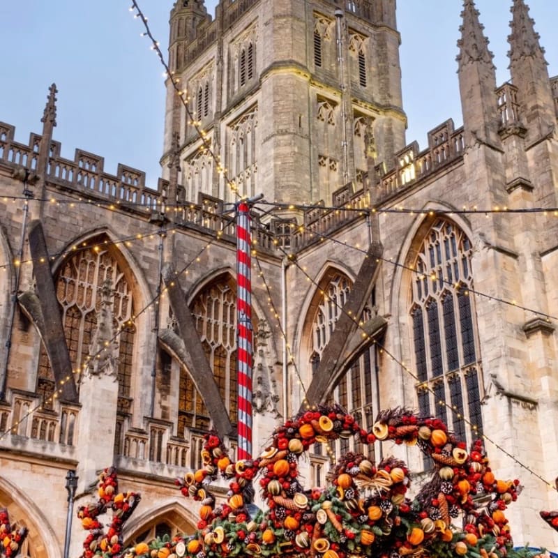 Ornate Christmas decorations featuring dried fruit and greenery adorn the foreground, set against the grand Gothic architecture of a cathedral in the background, all illuminated by festive string lights.