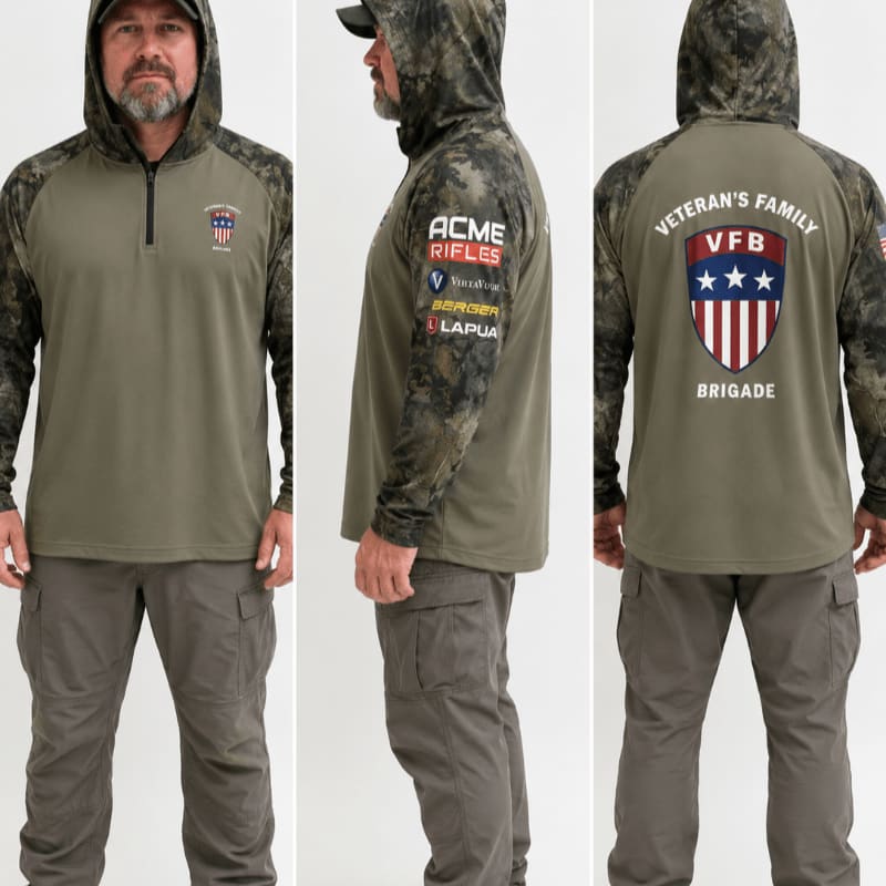 A man models a camouflage-sleeved, olive green hooded shirt with various logos on the front and back, paired with grey cargo pants, against a plain white background.