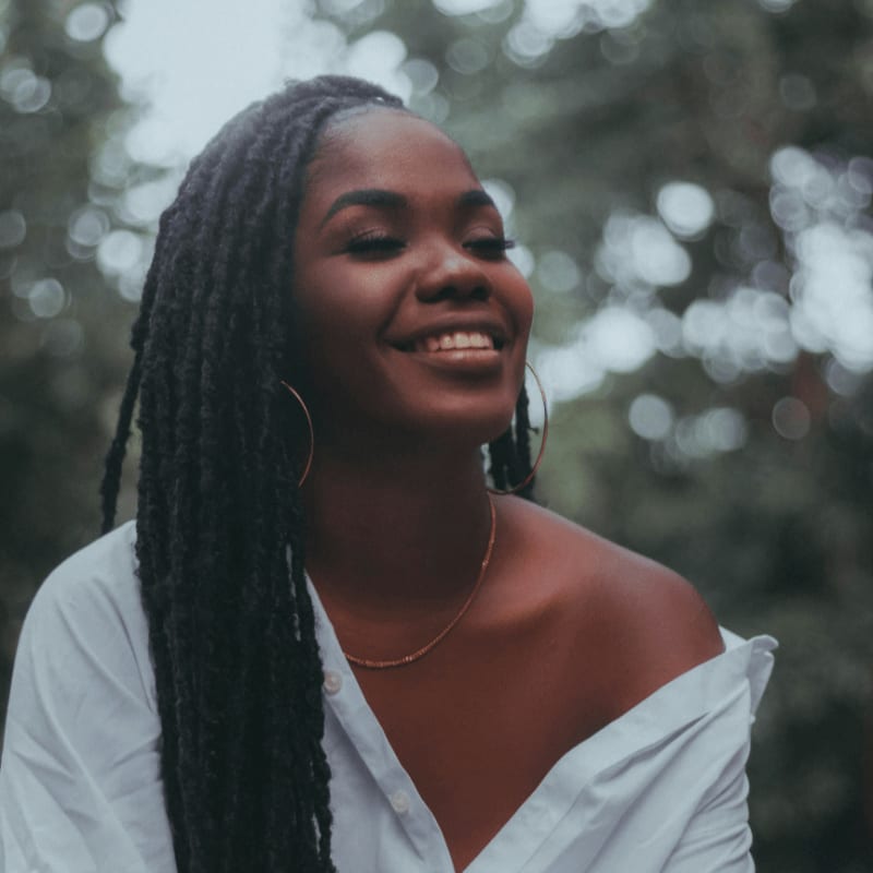 a woman with dreadlocks smiles while sitting in the woods