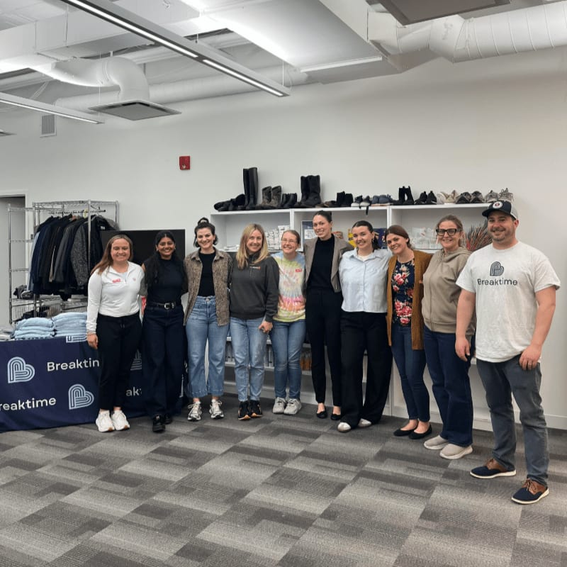 A group of people stand in front of a table with clothing and shoes displayed on shelves in the background.