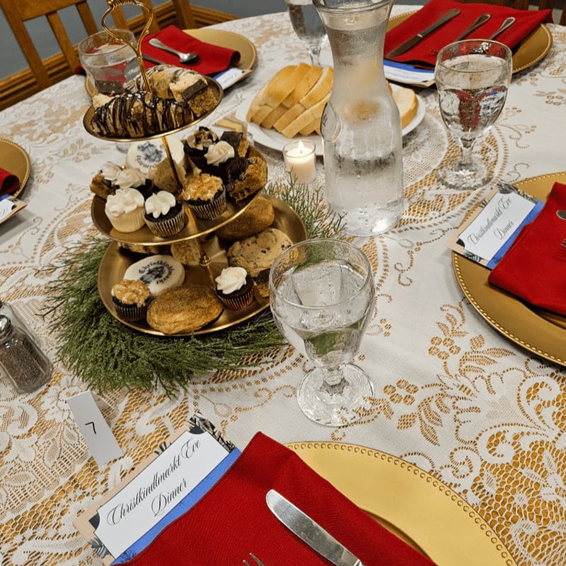 A festive table setting with a tiered dessert stand in the foreground and a pitcher of water and bread in the background.