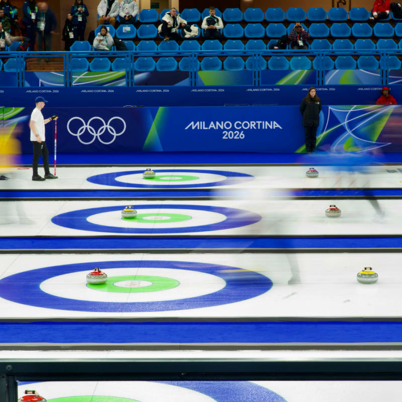 Curling match with athletes sliding stones on ice.
