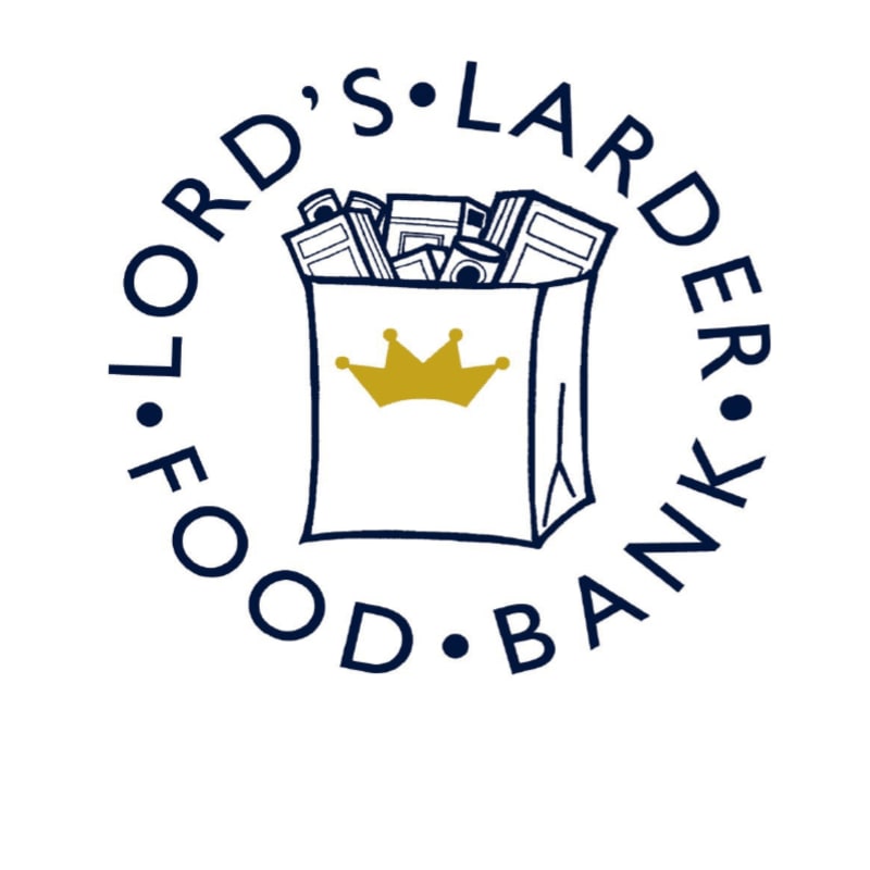 A white paper bag filled with groceries and adorned with a golden crown sits in the foreground, encircled by the words "L. FORD'S FOOD BANK" in dark blue lettering against a white background.