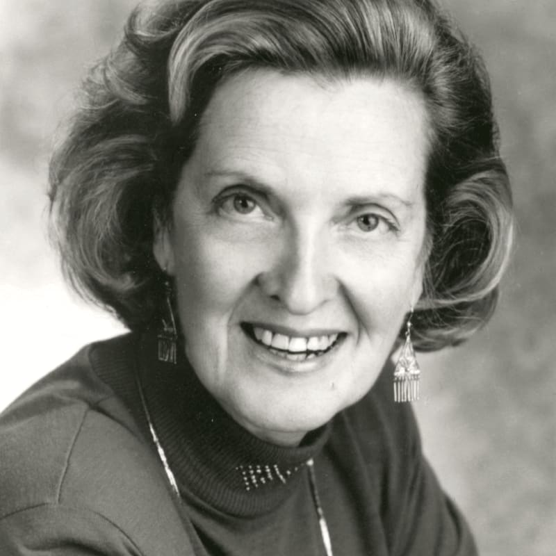A smiling woman with short, styled hair and dangling earrings is captured in a close-up shot against a softly blurred background.