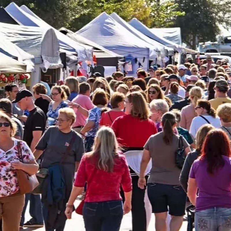A crowded outdoor market with white tents lining the background and people walking through the foreground.