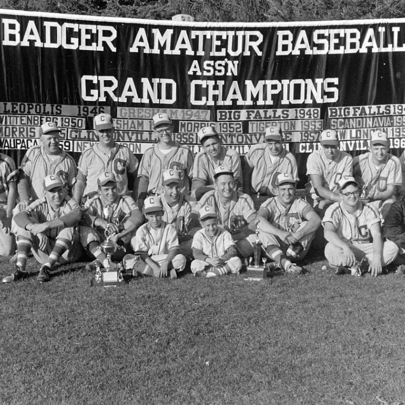 A group of young baseball players in uniform are posing for a photo on a grassy field in front of a banner proclaiming them "Grand Champions."