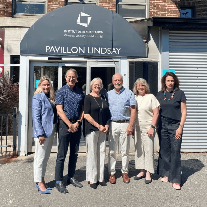 Six people stand in front of the "Pavillon Lindsay" entrance, with a brick building visible in the background.