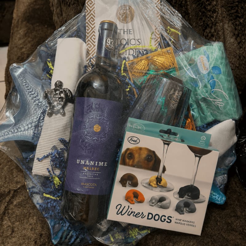 A gift basket filled with wine, a book, and dog-themed items sits on a brown fuzzy blanket.
