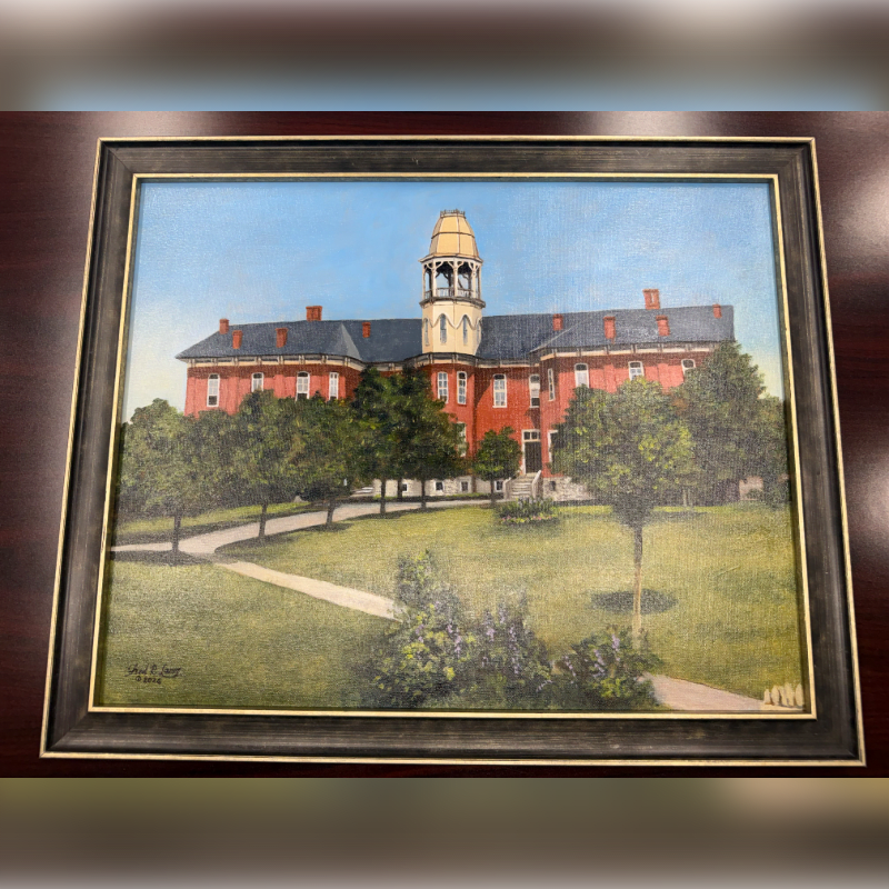 A framed painting displays a winding path through a grassy lawn in the foreground, leading to a large, red brick building with a prominent tower in the background.