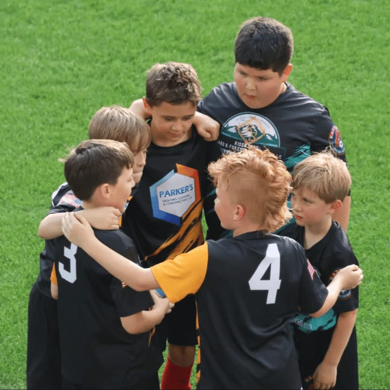 A group of young boys in soccer uniforms huddle together on a green field.