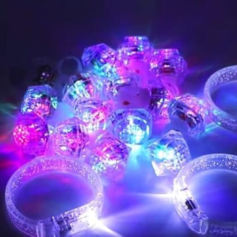 A pile of sparkling, colorful light-up rings and bracelets glows brightly against a dark, blurred background.