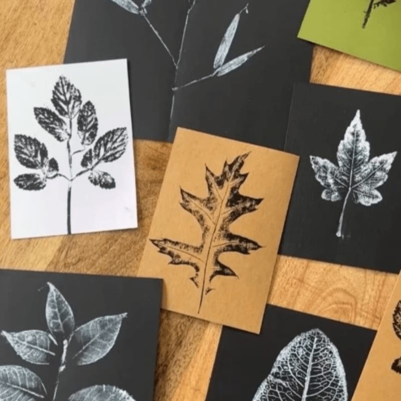 Several leaf prints on various colored paper are arranged on a wooden surface.