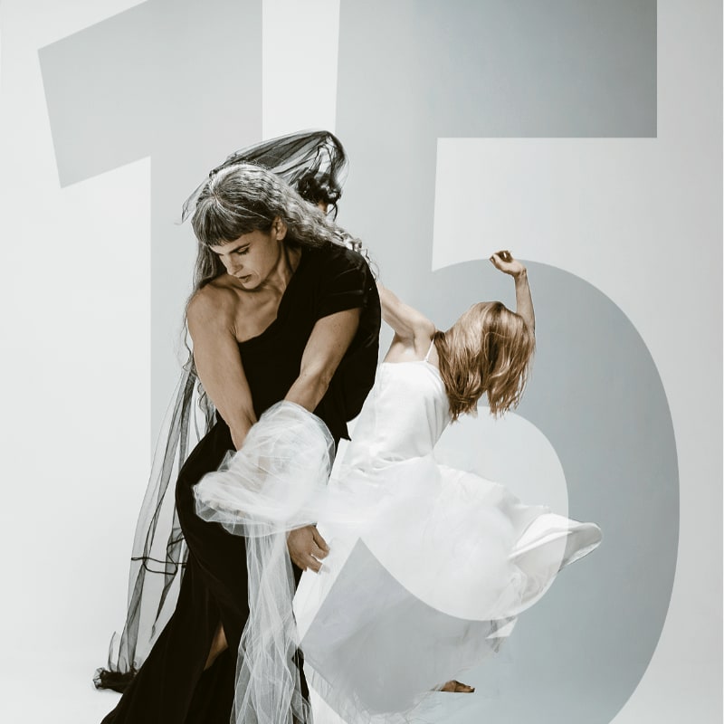 Two dancers in black and white attire are captured in a dynamic pose against a minimalist background featuring large, grey numerals.